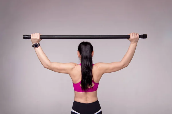 Красива м'язиста жінка робить вправи з гімнастичною палицею на сірому фоні . — стокове фото