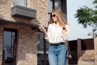 Beyaz gömlek ve patron gözlük yönetmen sevimli bir çekici çekici neşeli kız Portresi, iş merkezinin girişine yakın duran ve telefondan Sms arama.