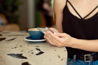 Cep telefonu tutan kadın ellerinin yakın çekim, kız rahat bir kafede bir mola sırasında cep telefonu videoları izlerken kahve içerken oturur.