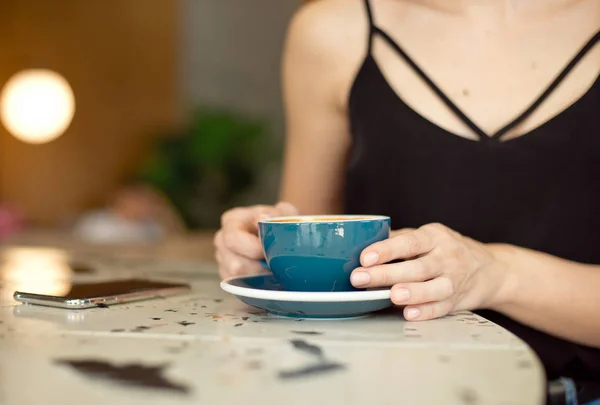 Nahaufnahme weiblicher Hände, die ein Mobiltelefon halten, Mädchen sitzt in einem gemütlichen Café und trinkt Kaffee und schaut sich während einer Pause Videos auf einem Mobiltelefon an. — Stockfoto