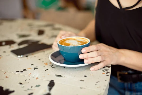 Primo piano di mani femminili in possesso di un telefono cellulare, la ragazza si siede in un accogliente caffè bere caffè guardando video su un telefono cellulare durante una pausa . — Foto Stock