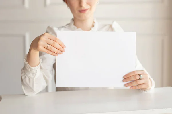 Woman holding white business card on white wall background.