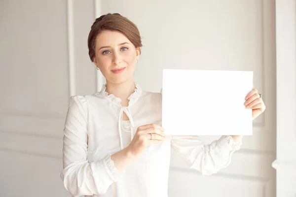 Jovem mulher sorrindo segurando uma folha de papel em branco para anunciar.Menina mostrando banner com espaço de cópia — Fotografia de Stock