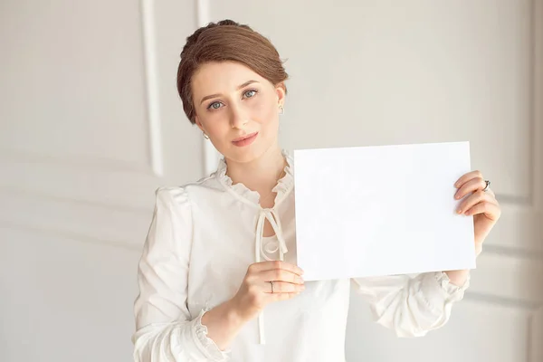 Jovem mulher sorrindo segurando uma folha de papel em branco para anunciar.Menina mostrando banner com espaço de cópia — Fotografia de Stock