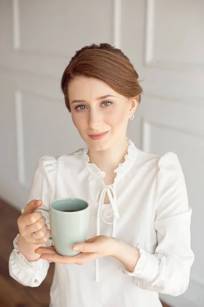Привлекательная молодая женщина в повседневной одежде держит чашку, смотрит в сторону и улыбается, на белом фоне . — стоковое фото