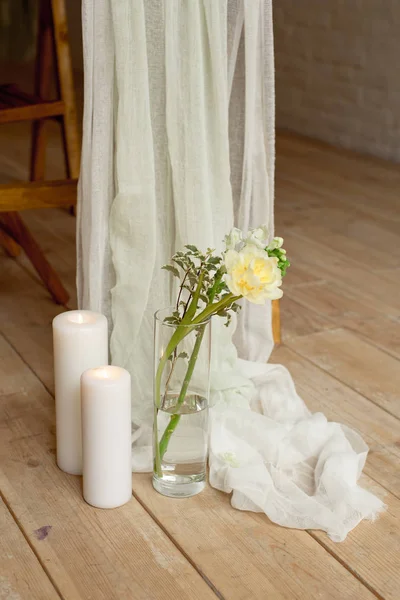 Branch of blooming white peony tulip Mattiola branch in a glass vase white wax candles stand on the wooden light floor indoors. — Stock Photo, Image