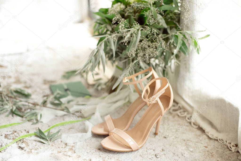 Wedding details, green bridal bouquet, shoes on a concrete window-sill of a pan-window.