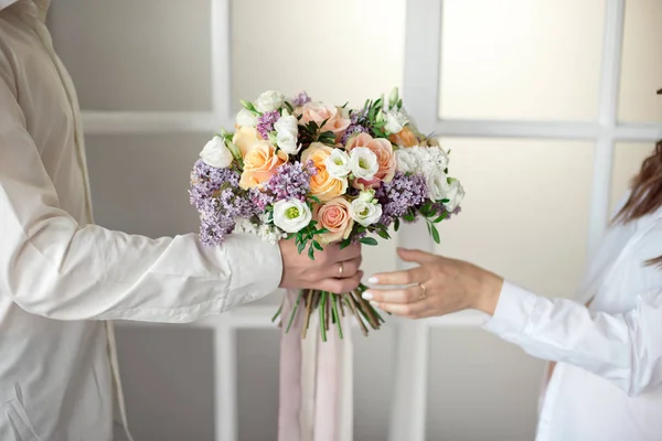Man stretches out his hands and gives a large bouquet of flowers from roses and lilacs isolated against the background of a stained glass window. Close-up female hands take a bouquet. Gift for March