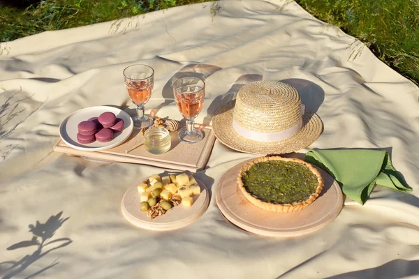 Picnic basket with fruit and macaroon bakery transparent glasses of drink on a beige fabric in the garden.