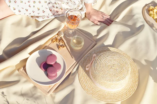 Picnic basket with fruit and bakery on red cloth in gardenmacaroon bakery transparent glasses of drink on a beige fabric in the garden