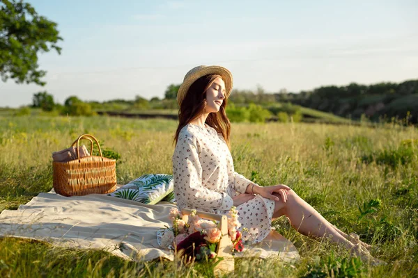 ハッピーウーマンライフスタイル、柔らかい夕日の光の中で自然のピクニックバスケットの花の藁帽子の美しいリラックスした女の子、ピクニック-キャンプ — ストック写真