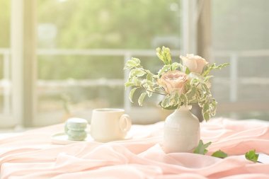 French blue macaroon plate and coffee cup standing on a wooden table with a pink tablecloth white vase with flowers roses and greens