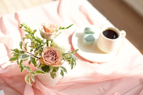 Mantel transparente rosa sobre una mesa blanca de madera una taza de café o té con macarrones franceses . —  Fotos de Stock