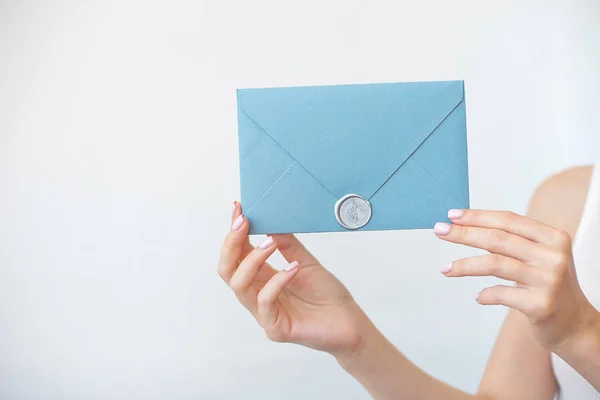 Foto de close-up de mãos femininas segurando um envelope de convite azul ou rosa prateado com um selo de cera, um certificado de presente, um cartão postal, um cartão de convite de casamento . — Fotografia de Stock