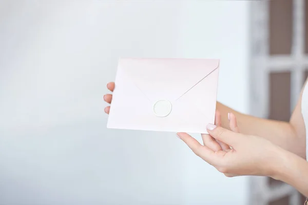 Foto de close-up de mãos femininas segurando um envelope de convite azul ou rosa prateado com um selo de cera, um certificado de presente, um cartão postal, um cartão de convite de casamento . — Fotografia de Stock