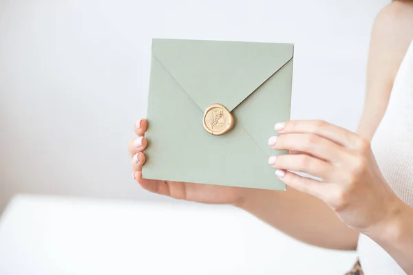 Foto de cerca de manos femeninas sosteniendo un sobre de invitación azul o rosa plateado con un sello de cera, un certificado de regalo, una postal, una tarjeta de invitación de boda . —  Fotos de Stock