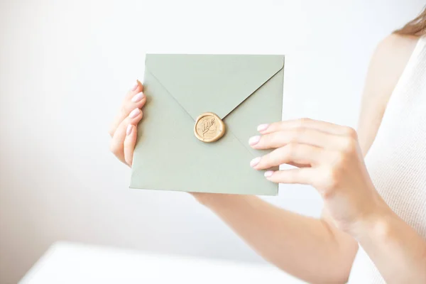 Close-up photo of female hands holding a silver blue or pink invitation envelope with a wax seal, a gift certificate, a postcard, a wedding invitation card.