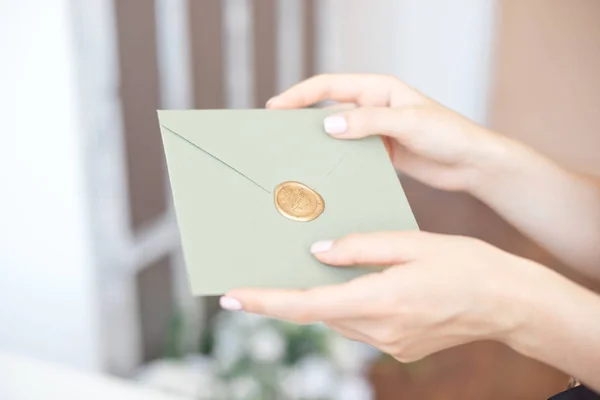 Close-up photo of female hands holding a silver blue or pink invitation envelope with a wax seal, a gift certificate, a postcard, a wedding invitation card.