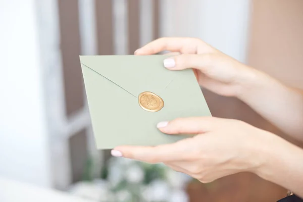 Foto de close-up de mãos femininas segurando um envelope de convite azul ou rosa prateado com um selo de cera, um certificado de presente, um cartão postal, um cartão de convite de casamento . — Fotografia de Stock