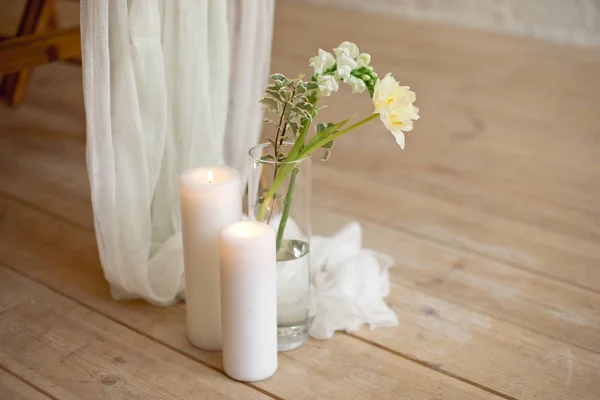 Rama de florecimiento tulipán blanco peonía Mattiola rama en un jarrón de vidrio velas de cera blanca de pie en el suelo de madera de luz en el interior . — Foto de Stock