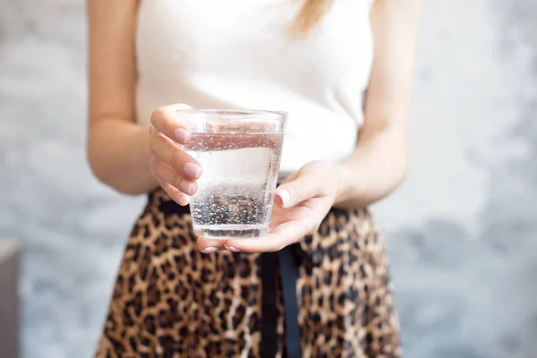 Girl in white top and skirt with a trendy print holds a glass of clean water to maintain the body's health and water balance. — Stock Photo, Image