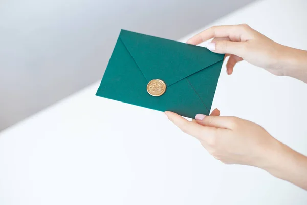 Foto de close-up de mãos femininas segurando um envelope de convite verde com um selo de cera, um certificado de presente, um cartão postal, um cartão de convite de casamento . — Fotografia de Stock