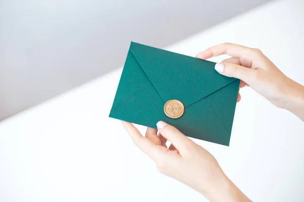 Nahaufnahme von weiblichen Händen mit einem grünen Einladungsumschlag mit Wachssiegel, einem Gutschein, einer Postkarte, einer Hochzeitseinladungskarte. — Stockfoto