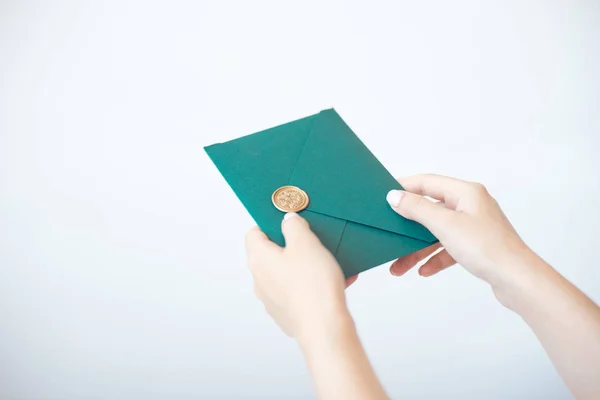 Close-up photo of female hands holding a green invitation envelope with a wax seal, a gift certificate, a postcard, a wedding invitation card.
