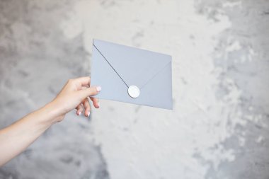 Kadın el gümüş zarf gri bir arka plan üzerinde bir düğün davetiyesi tebrik kartı verir.