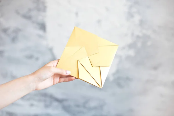 Женская рука дает золотой конверт квадратной формы свадебная открытка приглашения на сером фоне . — стоковое фото