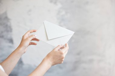 Yakın çekim kız gri bir arka plan üzerinde beyaz bir zarf düğün davetiyesi bildirimi iki eliyle tutar