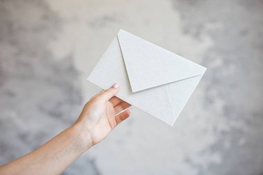 Kadın el beyaz zarf gri bir arka plan üzerinde bir düğün davetiyesi verir