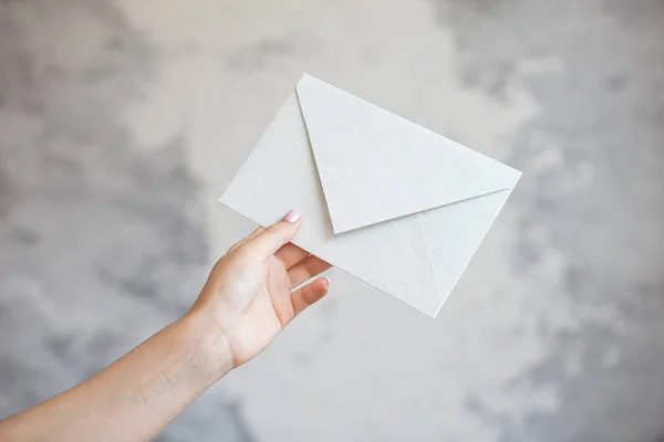 Female hand gives white envelope a wedding invitation on a gray background