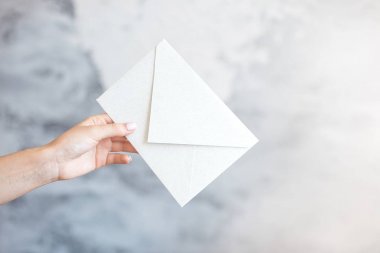 Kadın el beyaz zarf gri bir arka plan üzerinde bir düğün davetiyesi verir