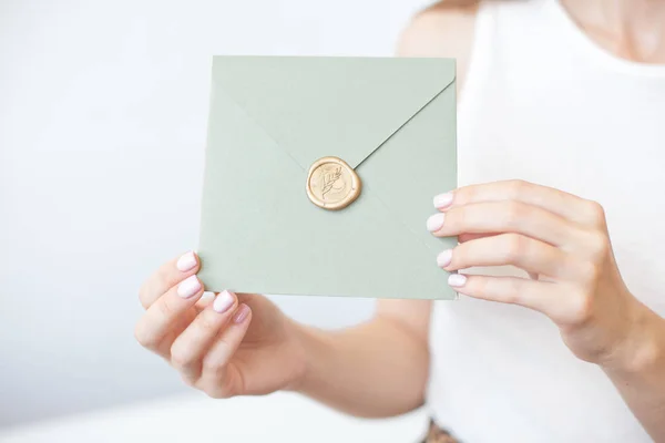 Foto de close-up de mãos femininas segurando um envelope de convite de prata com um selo de cera, um certificado de presente, um cartão postal, um cartão de convite de casamento . — Fotografia de Stock