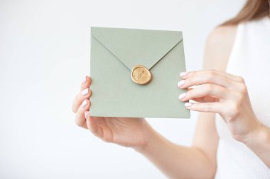 Balmumu mührü, hediye çeki, kartpostal, düğün davetiyekartı ile zeytin davetiye zarfı tutan kadın ellerinin yakın çekim fotoğrafı.