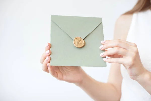Nahaufnahme von weiblichen Händen mit einem olivgrünen Einladungsumschlag mit Wachssiegel, einem Gutschein, einer Postkarte, einer Hochzeitseinladungskarte. — Stockfoto