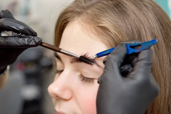 Beautiful woman drawing a shape of eyebrows using cosmetic brush. Make up artist applying make up to a model. — Stock Photo, Image