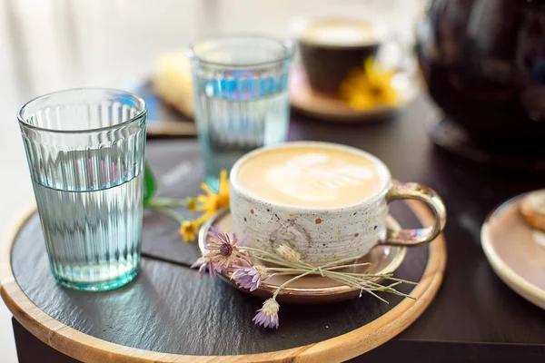 Different types of coffee in a cup on a dark table, two glasses with cold water and spring flowers on the table, top view.