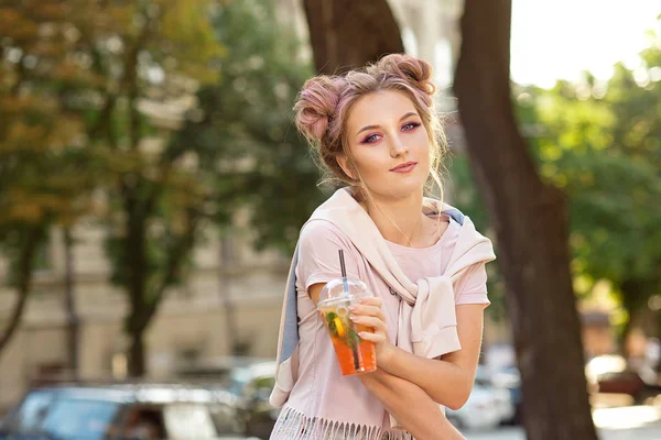 屋外散歩の後、プラスチック製のテイクアウトフードカップから新鮮なジュースを飲む若い美しい女の子。健康的なライフスタイル。ピンクの髪でスリムなブロンドを微笑む. — ストック写真