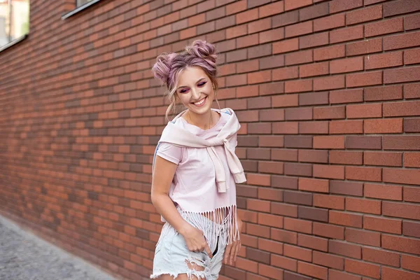 Portrait of a young beautiful girl with pink hair bun smiling against a red brick wall — Stock Photo, Image