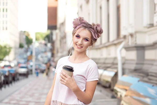 Sorrindo menina bonita com cabelo rosa penteado caminha pela rua com uma xícara de café desfrutando de um belo dia ensolarado . — Fotografia de Stock