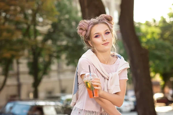 ピンクのTシャツと明るいメイクアップとヘアバンズと夏のカクテルで外に座ってスウェットシャツで幸せな若い笑顔の女の子 — ストック写真