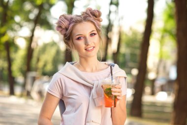 Genç güzel kız açık havada bir yürüyüşe sonra Plastik paket gıda bardak taze meyve içme. Sağlıklı bir yaşam tarzı. Pembe saç ile gülümseyen ince sarışın