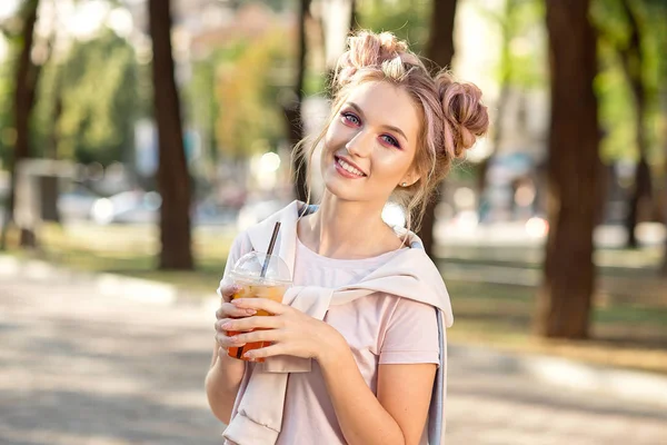 Genç güzel kız açık havada bir yürüyüşe sonra Plastik paket gıda bardak taze meyve içme. Sağlıklı bir yaşam tarzı. Pembe saç ile gülümseyen ince sarışın