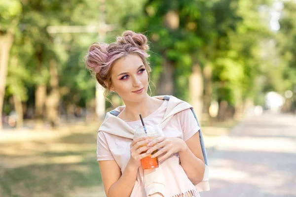 屋外散歩の後、プラスチック製のテイクアウトフードカップから新鮮なジュースを飲む若い美しい女の子。健康的なライフスタイル。ピンクの髪でスリムなブロンドを微笑む — ストック写真