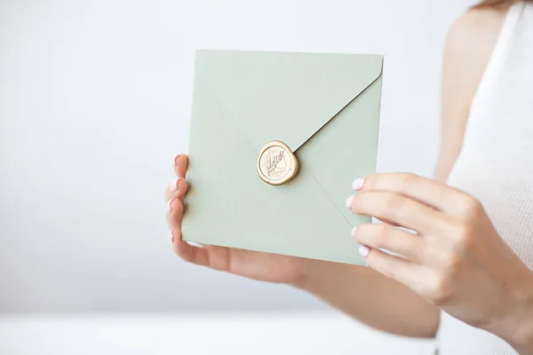 Close-up photo of female hands holding invitation envelope with a gold wax seal, a gift certificate, a postcard, wedding invitation card