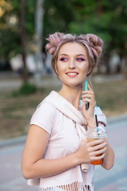 Genç güzel kız açık havada bir yürüyüşe sonra Plastik paket gıda bardak taze meyve içme. Sağlıklı bir yaşam tarzı. Pembe saç ile gülümseyen ince sarışın