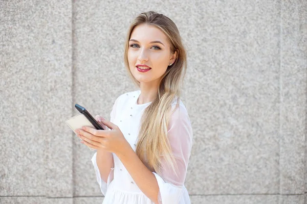 Sokakta duran akıllı telefonu olan mutlu genç kız arkadaşlarına mesaj yazıyor.