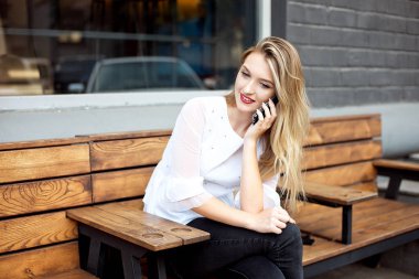 Güzel bir gülümseme ile Charming kadın bir kafede dinlenirken bir cep telefonu iyi haber konuşuyor, mutlu bir Kafkas kadın boş zamanlarında bir kafede dinlenirken bir cep telefonu konuşuyor.